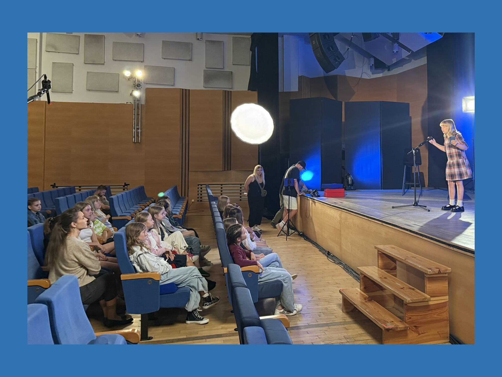 kadr ze spotu - sala ze sceną i widownią pełną ludzi